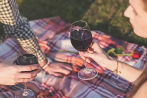 couple outdoors on a picnic blanket holding wine glasses